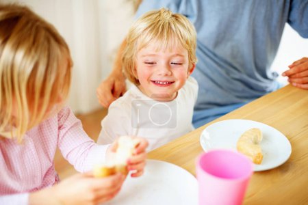 Foto de Feliz, cocina y niños desayunando juntos para una comida saludable, de bienestar y dieta. Sonríe, ríe y los hermanos pequeños se unen y disfrutan de un almuerzo o brunch junto a una mesa de madera en la casa familiar moderna - Imagen libre de derechos