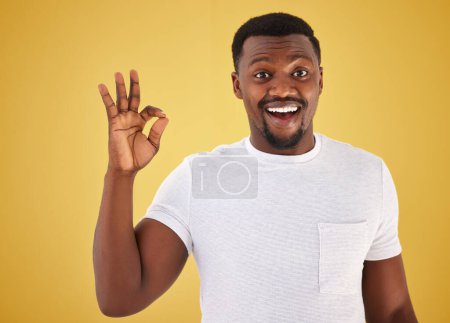 Foto de Hombre africano, signo de ok y retrato de estudio para la sonrisa, wow y sorpresa para la revisión, voto o como por el fondo amarillo. Persona, mano y emoji para retroalimentación, elección o decisión con icono, símbolo y feliz. - Imagen libre de derechos