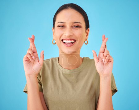Photo for Woman, cross fingers and studio portrait for smile, emoji or sign for hope by blue background. Girl, person and hands for good luck, wish or excited with icon, symbol or faith for results in contest. - Royalty Free Image