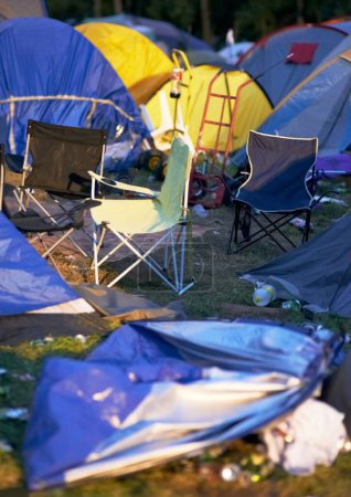 Téléchargez les photos : Tentes, poubelles et déchets lors d'un festival de musique en plein air ou d'un événement pour une fête ou un rassemblement social. Été, camping et poubelles avec matériel de camping désordonné, chaises ou boîtes froides sur le terrain. - en image libre de droit