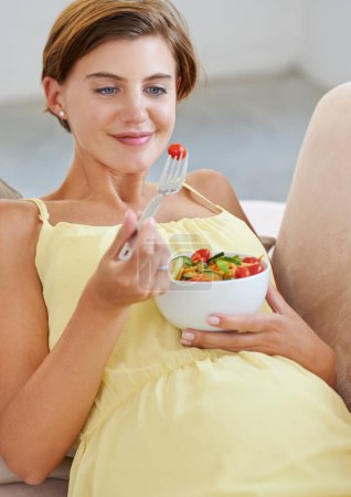 Foto de Mujer embarazada, ensalada y sonrisa en sofá para la salud, nutrición y bienestar en la sala de estar del apartamento. Persona, verduras o feliz en el sofá del salón para relajarse, embarazo y dieta saludable con fibra. - Imagen libre de derechos