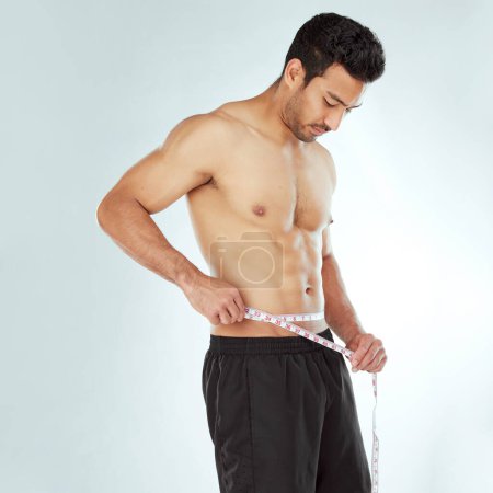 Photo for Stomach, measuring tape and fitness man in studio with Weight loss, progress or bmi control on white background. Body, wellness and male model with waist measurement for diet, health or sixpack check. - Royalty Free Image