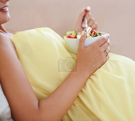 Foto de Mujer embarazada, ensalada y cuenco en sofá para la salud, nutrición y bienestar en la sala de estar del apartamento. Persona, fruta y feliz en el sofá del salón para relajarse, embarazo y dieta saludable con vitaminas. - Imagen libre de derechos