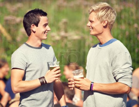 Photo for Men, talking and drinks in summer with beer, alcohol and happiness at outdoor, music festival or event. Happy, conversation and friends in park for concert, celebration and drinking together in woods. - Royalty Free Image