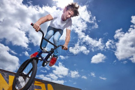 Téléchargez les photos : Vélo, saut et adolescent sur la rampe pour la performance sportive, monter ou s'entraîner pour l'événement au parc avec ciel. Équilibre vélo, cascade ou enfant sur le bord de la planche pour un tour de vélo en compétition ou un défi avec risque. - en image libre de droit