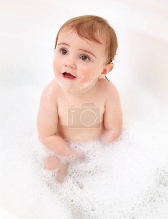 Photo for Baby in bathtub with foam, water and clean fun in home for skincare, wellness and hygiene. Bubble bath, soap and happy child in bathroom with cute face, care and washing body of dirt, germs and smile. - Royalty Free Image