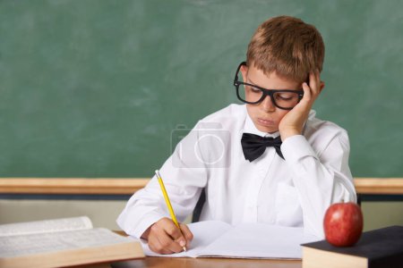 Photo for Frustrated boy child, classroom and writing in books for knowledge, information and studying at academy. Student kid, learning and education with glasses, thinking and stress with dyslexia at school. - Royalty Free Image