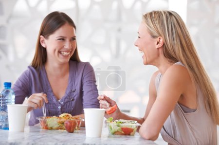 Foto de Ensalada, amigos o mujeres en el almuerzo para la felicidad o sonreír en el descanso para relajarse juntos para bromas divertidas. Conversación, saludable o compañeros riéndose a la mesa en la cafetería para comer fruta o comunicación. - Imagen libre de derechos