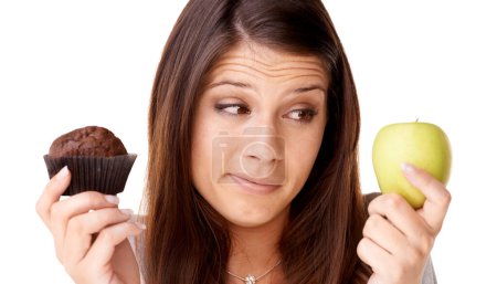 Photo for Face, choice and apple or muffin with a woman in studio isolated on a white background for food decision. Doubt, health or nutrition with a confused young person holding fruit and dessert options. - Royalty Free Image