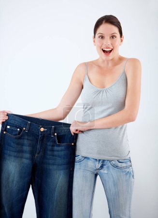 Photo for Surprise, weight loss and woman with jeans, change in size and white background in studio. Wow, shocked and portrait of person with crazy reaction to transformation in fitness or large denim pants. - Royalty Free Image
