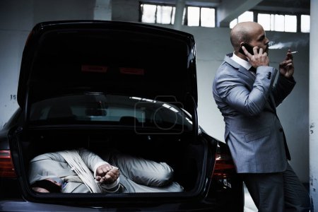 Photo for Phone call, car and gangster with hostage in trunk for negotiation, kidnapping danger and crime. Mafia, ransom criminal and business person in boot for abduction, money and terrorism in parking lot. - Royalty Free Image