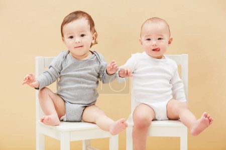 Photo for Portrait, chair and baby boys for growth or child development in studio on an orange background. Children, cute or adorable and sibling or small infant kids sitting together for family bonding. - Royalty Free Image