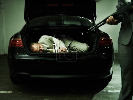 Photo for Man in trunk of car, kidnapping and gun with mafia, danger and violence in basement garage. Crime, human trafficking and scared person tied with rope parking lot with gangster, robbery and terror - Royalty Free Image
