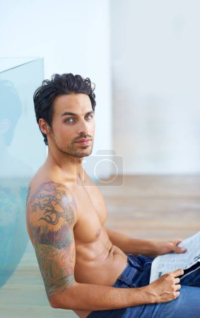 Photo for Man, newspaper and shirtless or portrait for news, article or story on floor with relax and calm expression. Person, face and information update or break with tattoo, peace or routine in apartment. - Royalty Free Image