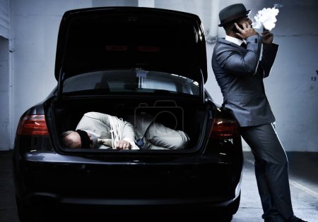 Photo for Crime, car and man with hostage in trunk for negotiation, kidnapping ransom and phone call. Mafia, gangster criminal and businessman smoking in boot for abduction, danger and robbery in parking lot. - Royalty Free Image