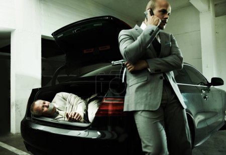 Photo for Phone call, car and man with hostage in trunk for negotiation, kidnapping danger and crime. Mafia, gangster criminal and business person in boot for financial crisis, debt and payment in parking lot. - Royalty Free Image