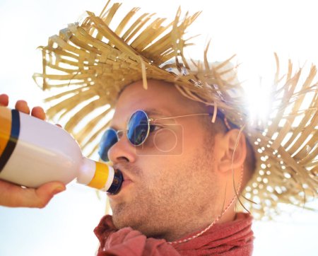 Photo for Man, drinking and alcohol with sunlight outdoor for concert, event or music festival with sunglasses and straw hat. Person, drink and beverage in summer for relax, freedom and enjoyment with sunshine. - Royalty Free Image