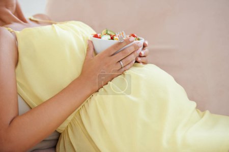 Foto de Mujer embarazada, comiendo ensalada y sofá de la sala de estar, solo y disfrutando de un delicioso antojo de embarazo. Bienestar relajado, vegetal y de maternidad con comida saludable y satisfacción nutricional. - Imagen libre de derechos