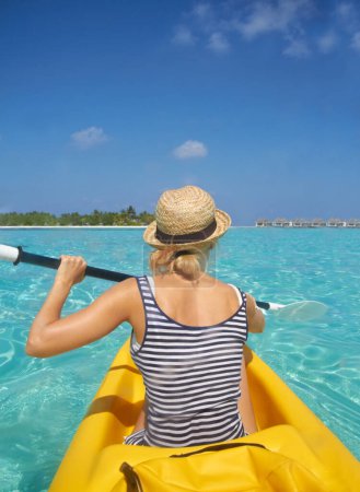 Téléchargez les photos : Femme, kayak et océan tropical en été en chapeau, espace maquette ou fond bleu ciel par île. Personne, bateau ou retour pour le transport, vacances ou voyage en vacances au soleil, l'eau ou la mer pour l'aviron. - en image libre de droit