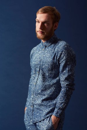 Photo for Man, fashion and chic clothes in studio with unique style, denim and trendy on blue background. Irish odel with hipster beard, red hair with serious face and stylish, fashionable shirt and jeans. - Royalty Free Image