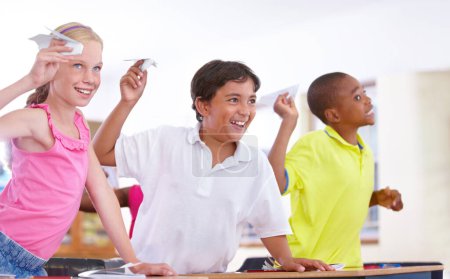 Téléchargez les photos : Enfants heureux, étudiants et avion en papier en classe en pause au bureau pour des jeux amusants à lancer ou à se détendre. Diversité, distraction ou enfants jouant avec le sourire, l'origami ou l'avion à l'école ensemble. - en image libre de droit