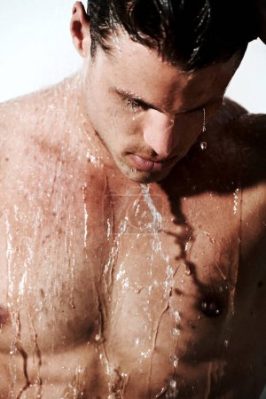Photo for Serious, man in shower to relax and washing body for hygiene, morning wellness and skin routine. Grooming, skincare and face of male model with muscle cleaning in water, self care and calm bathroom - Royalty Free Image
