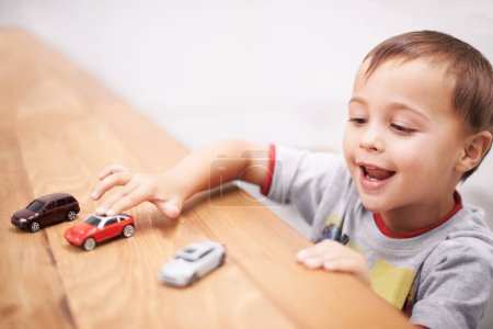 Photo for Cars, toys and boy kid by table playing for learning, development and fun at modern home. Cute, sweet and young child enjoying a game with plastic vehicles by wood for childhood hobby at house - Royalty Free Image
