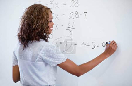 Photo for Woman, teacher and writing on whiteboard for maths, numbers or equations in classroom. Rear view of female person, educator or lecturer with sum on board for learning or problem solving in class. - Royalty Free Image