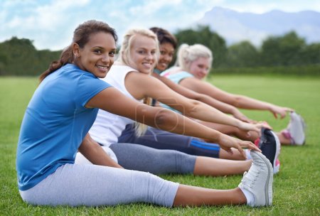Foto de Mujeres, piernas estiradas y fitness en parque, campo deportivo y naturaleza con ejercicio para la salud y el bienestar. El grupo de atletas se calienta para entrenar, entrenar juntos y retratar con sonrisa al aire libre. - Imagen libre de derechos