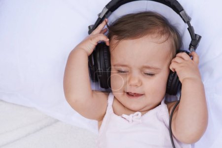 Foto de Bebé, auriculares y música en streaming para relajarse, radio y escuchar podcast en la cama en casa. Sonido de niña, niño y audición para el desarrollo o el aprendizaje infantil, lista de reproducción infantil y calmante para audio. - Imagen libre de derechos