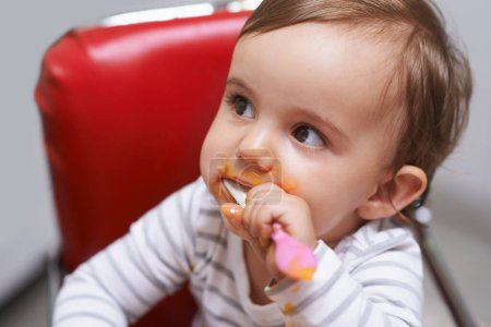 Téléchargez les photos : Manger, bébé mignon et garçon dans une chaise avec de la nourriture végétale pour le développement de l'enfant à la maison. Doux, nutritionnel et affamé jeune enfant ou tout-petit profiter d'un déjeuner sain, dîner ou souper repas à la maison - en image libre de droit
