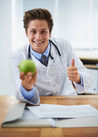 Photo for Thumbs up, apple and portrait of man doctor with stethoscope for positive, good and confident attitude. Happy, smile and young healthcare worker with fruit in medical office of hospital or clinic - Royalty Free Image