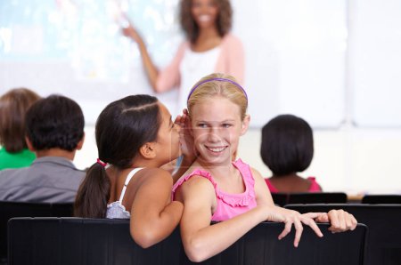 Photo for Kids, classroom and whisper in ear for secret, gossip or communication in lesson at school. Little girl, students or friends listening to rumor, information or surprise in class together with teacher. - Royalty Free Image