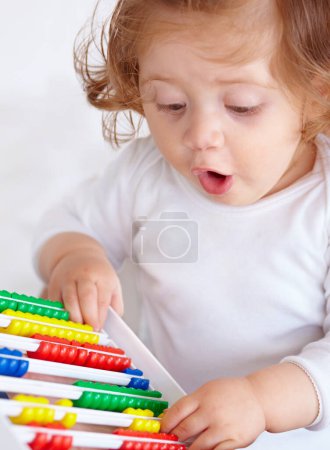 Photo for Abacus, surprise and girl baby learning, playing and teaching for child development on bed. Maths, toy and closeup of young kid, infant or toddler counting for education in bedroom at modern home - Royalty Free Image