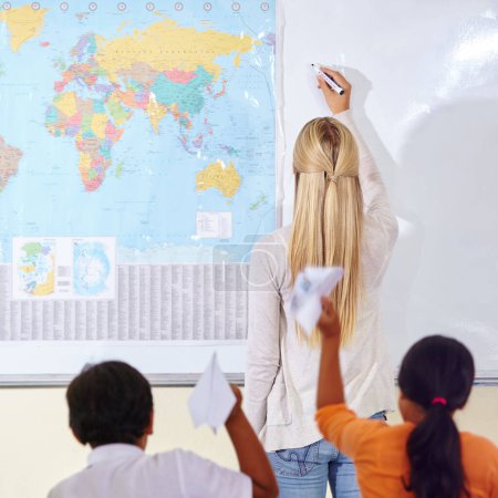 Photo for Teacher, woman and children in a classroom, learning and knowledge with information, paper planes and studying. Students, group and educator writing on a board, education and world map with school. - Royalty Free Image