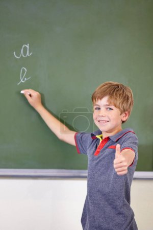 Photo for Portrait, child writing or thumbs up on chalkboard in classroom of elementary school. Boy, education student or happy kid with smile or hand gesture for like emoji, agreement or learning to write. - Royalty Free Image
