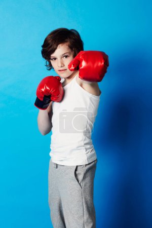 Photo for Portrait, boy and kid with boxing gloves, fitness and confident fist on a blue studio background. Child development, punch and fighting with workout, combat and training with fun and mockup space. - Royalty Free Image