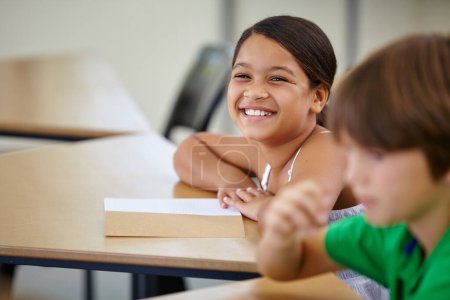 Photo for Portrait, children and girl in a classroom, education and relax with a book, learning and creative. Face, studying or students with joy, child development or desk with notes and knowledge in school. - Royalty Free Image