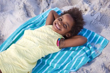 Photo for Happy, african child and portrait on beach sand, relax and summer holiday with sunshine in nature. Black girl, young and smile face on towel on vacation, cape town and seaside for wellness in outdoor. - Royalty Free Image
