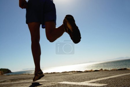 Photo for Person, running and asphalt at beach for fitness, workout or outdoor cardio training on a sunny day. Closeup of athlete legs on run, sprint or race on road or street by the ocean coast on mockup. - Royalty Free Image