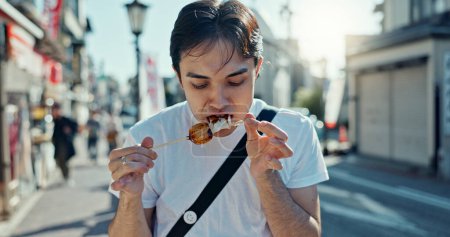 Téléchargez les photos : L'homme, la nourriture de rue et de manger du kebab sur la marche en voyage, en ville et affamés de goheimochi avec la nutrition, l'alimentation ou le déjeuner. Personne, collation de riz et brochette sur le trottoir du métro, vacances et route urbaine au Japon. - en image libre de droit