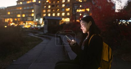 Foto de Mujer asiática, teléfono y noche en la ciudad para redes sociales, comunicación o redes al aire libre. Mujer persona relajarse en el teléfono inteligente móvil en la tarde por la noche para chatear en línea en la ciudad urbana de Japón. - Imagen libre de derechos
