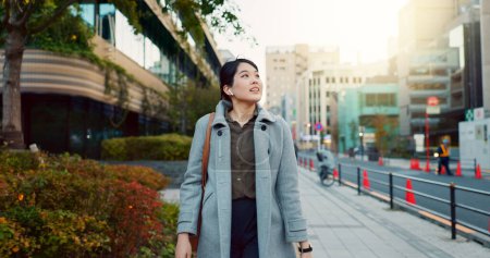 Photo for Woman, Asian and walking, travel or commute to work with professional in city with earphones. Listening to music on journey, podcast and commuter on urban street or sidewalk in Tokyo with playlist. - Royalty Free Image