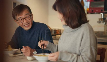 Photo for Japanese couple, food and home with conversation, love and bonding together with happiness, romance and smile. Apartment, old man or senior woman with healthy meal, nutrition and cheerful with dinner. - Royalty Free Image