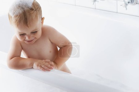 Téléchargez les photos : Bébé heureux dans la salle de bain avec savon, bulles et nettoyage sur maquette dans la routine du matin pour l'hygiène, le bien-être et les soins à la maison. Tout-petit lavant en mousse avec sourire, se détendre et rire enfant dans la baignoire dans la salle de bain. - en image libre de droit