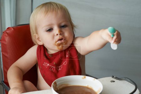 Photo for Feeding chair, eating and baby with spoon in a house for food, nutrition and fun while playing. Food, messy eater and boy kid at home with meal for child development, diet or nutrition while learning. - Royalty Free Image