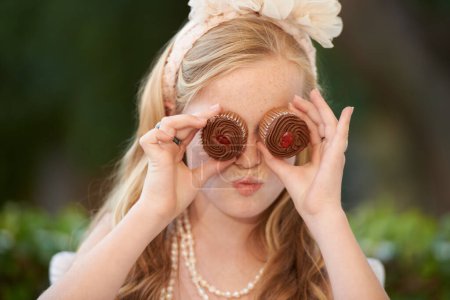 Photo for Child, cupcakes and eyes for fun play or dress up in garden for birthday celebration, dessert or event. Female person, fancy accessories and funny face with sweet food or outdoor, quirky or humor. - Royalty Free Image