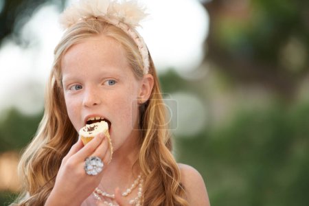 Photo for Child, girl and eating cupcake or garden for birthday food or celebration, dessert or candy. Female person, happy kid and bite sweet snack at outdoor event for hungry joy or treat meal, party or fun. - Royalty Free Image