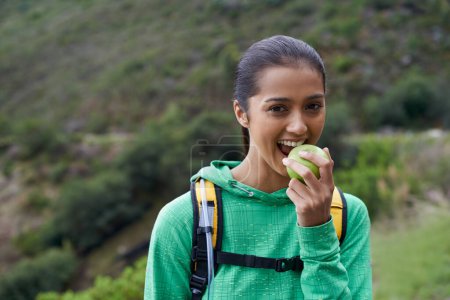 Téléchargez les photos : Manger, fruits et randonnée portrait de la femme dans le parc, la nature ou la pomme dans un sac à dos pour l'énergie. Heureux, trekking et affamé personne se détendre en plein air sur le sentier avec de la nourriture saine pour le bien-être sur l'aventure. - en image libre de droit