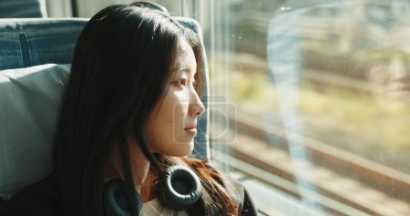 Téléchargez les photos : Femme japonaise, fenêtre et train avec écouteurs, Voyage et les transports en commun sur la balle de métro. Jeune, penser et se détendre sur un véhicule rapide pour le week-end et le bien-être par la technologie audio. - en image libre de droit